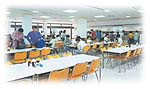 光が丘キャンパスの学生食堂で、学生たちが食事を楽しんでいる様子。明るい室内に多くのテーブルと椅子が配置されている。