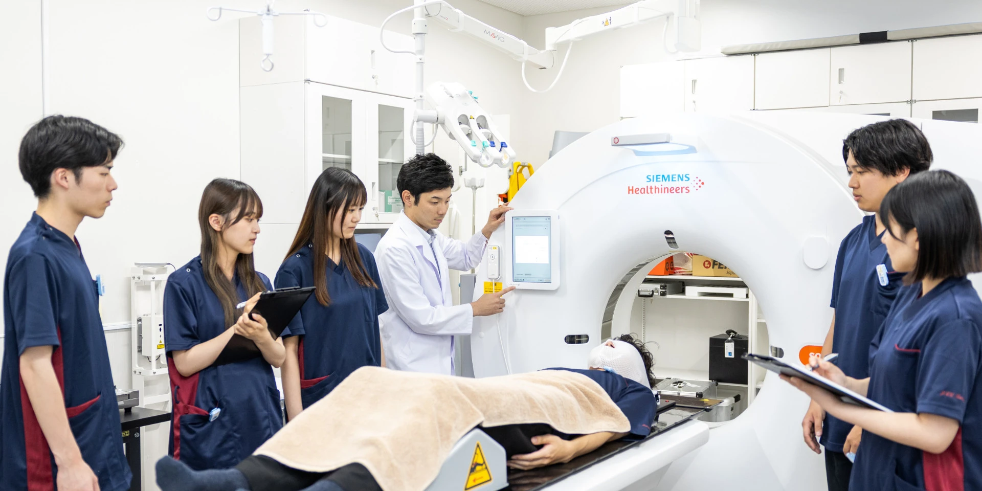 医療実習中の学生たちが、シミュレーターを使ってCTスキャンの手順を学んでいる様子（画像をクリックすると診療放射線科学科のページへ移動します）。