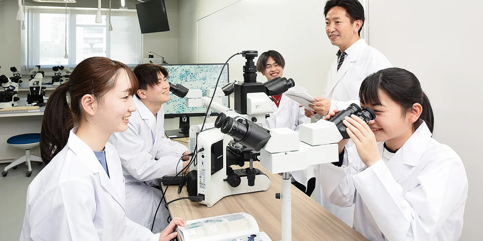 学生たちが顕微鏡を使って実習を行っている保健科学部の研究室の様子（画像をクリックすると臨床検査学科のページへ移動します）。